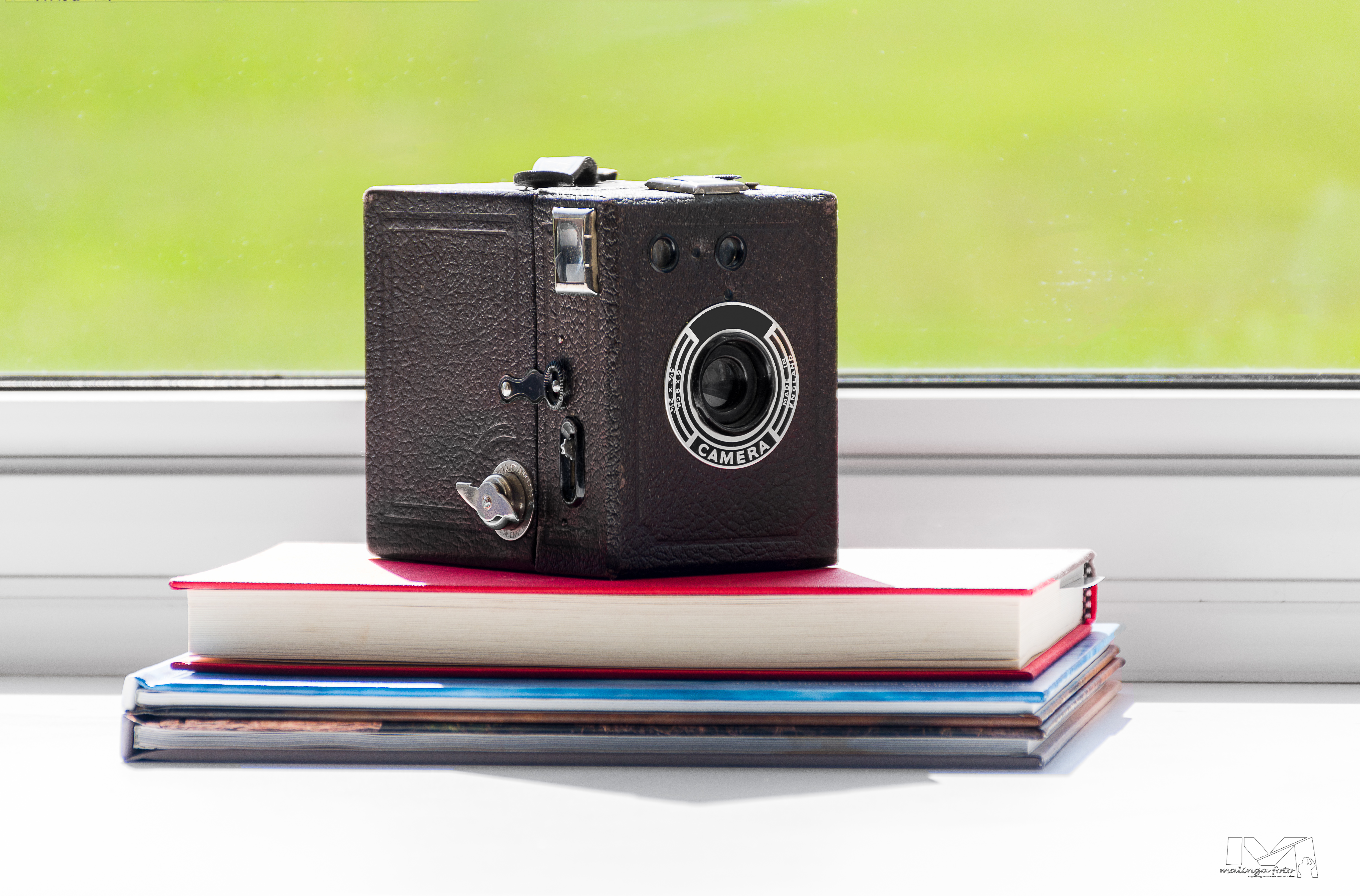 a vintage camera sitting on top of book in front of window